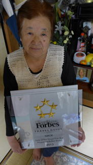 Kiyoshi Naoe holding the Forbes Travel Guide Five-Star Award next to a picture of Yasushi Naoe