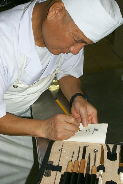 Yasushi Naoe signing a carving tool set for Kevin Cory in the kitchen of Kawai Ryokan, Toyama